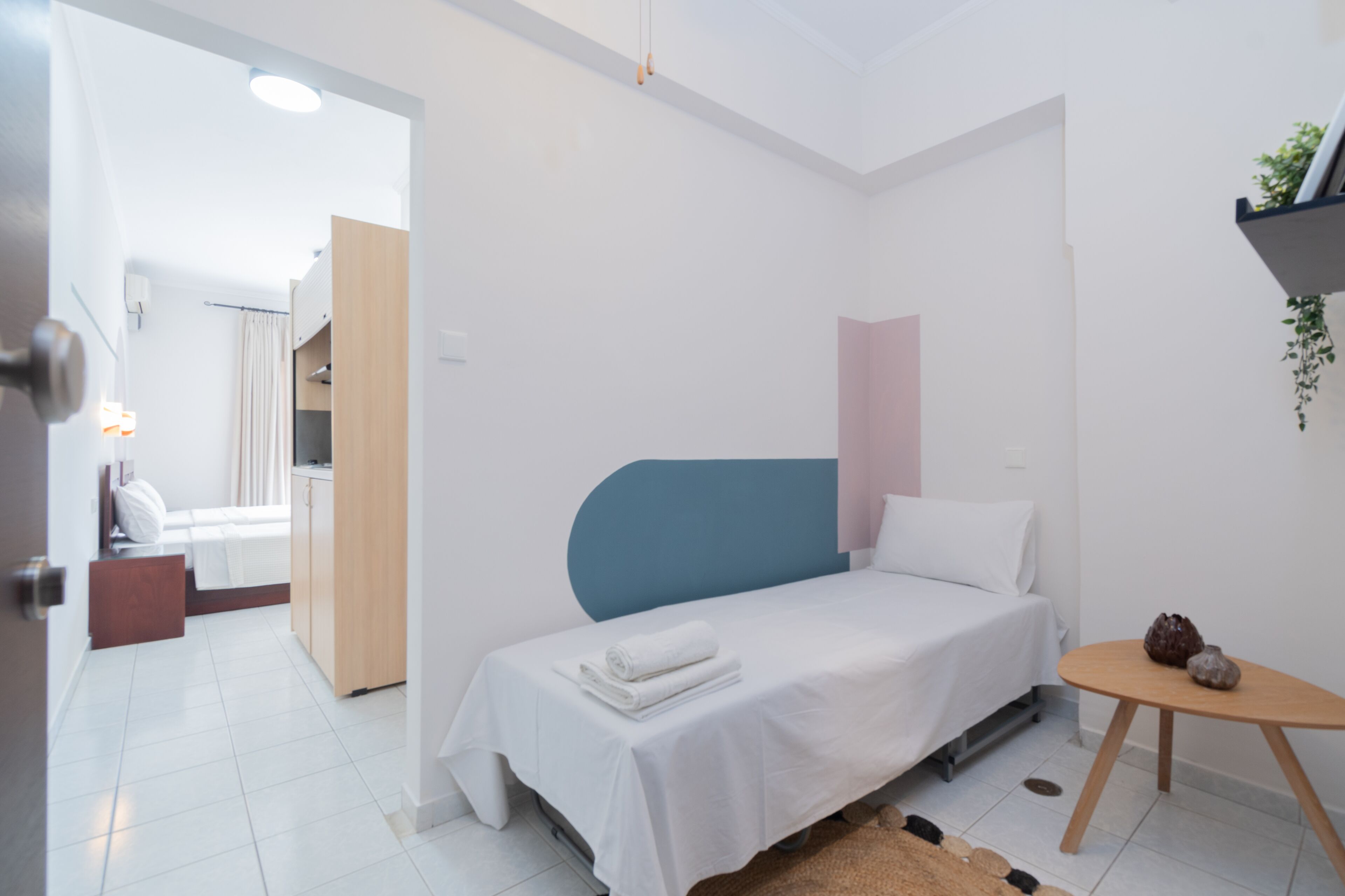A modern, well-lit bedroom with a single bed, a small table, and a shelf with a plant.