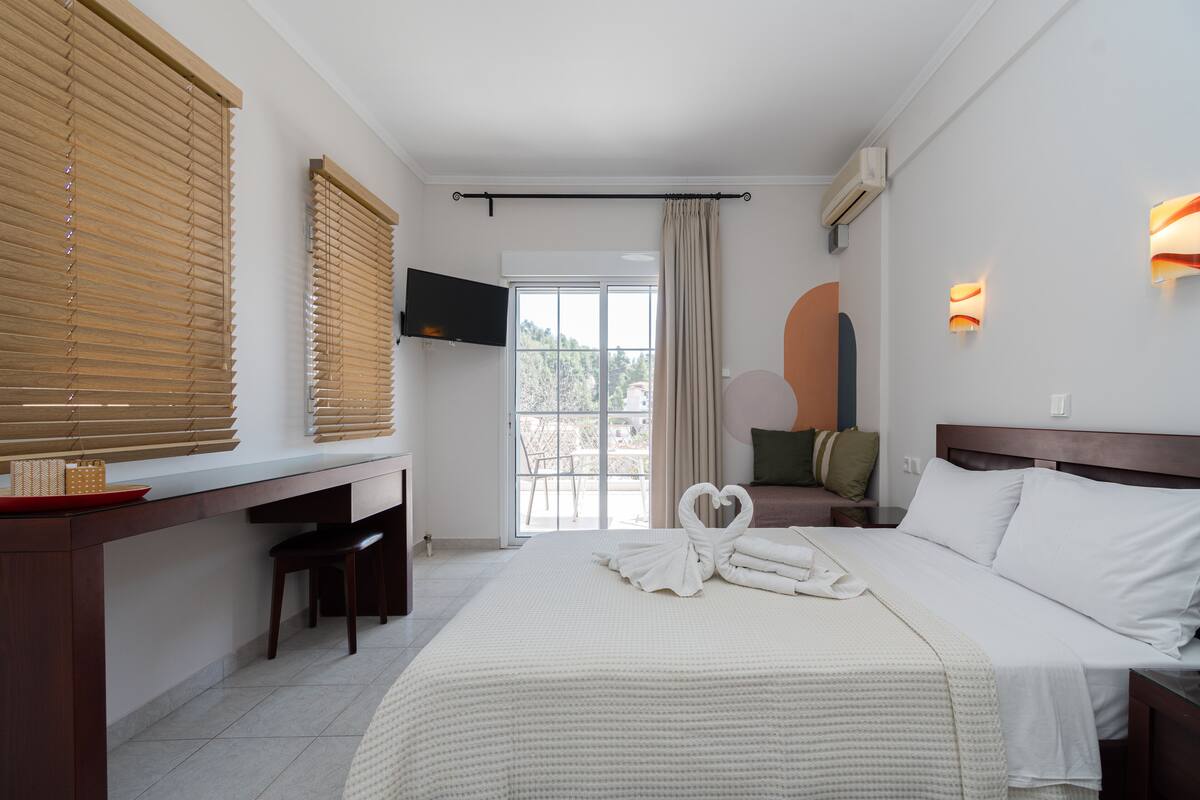 Ein Hotelzimmer mit Bett, Schreibtisch, Fernseher und einem Balkon mit Blick.