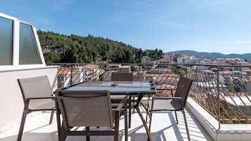 En terrasse med et bord og stole, med udsigt over et boligområde med huse og en bakke i baggrunden.