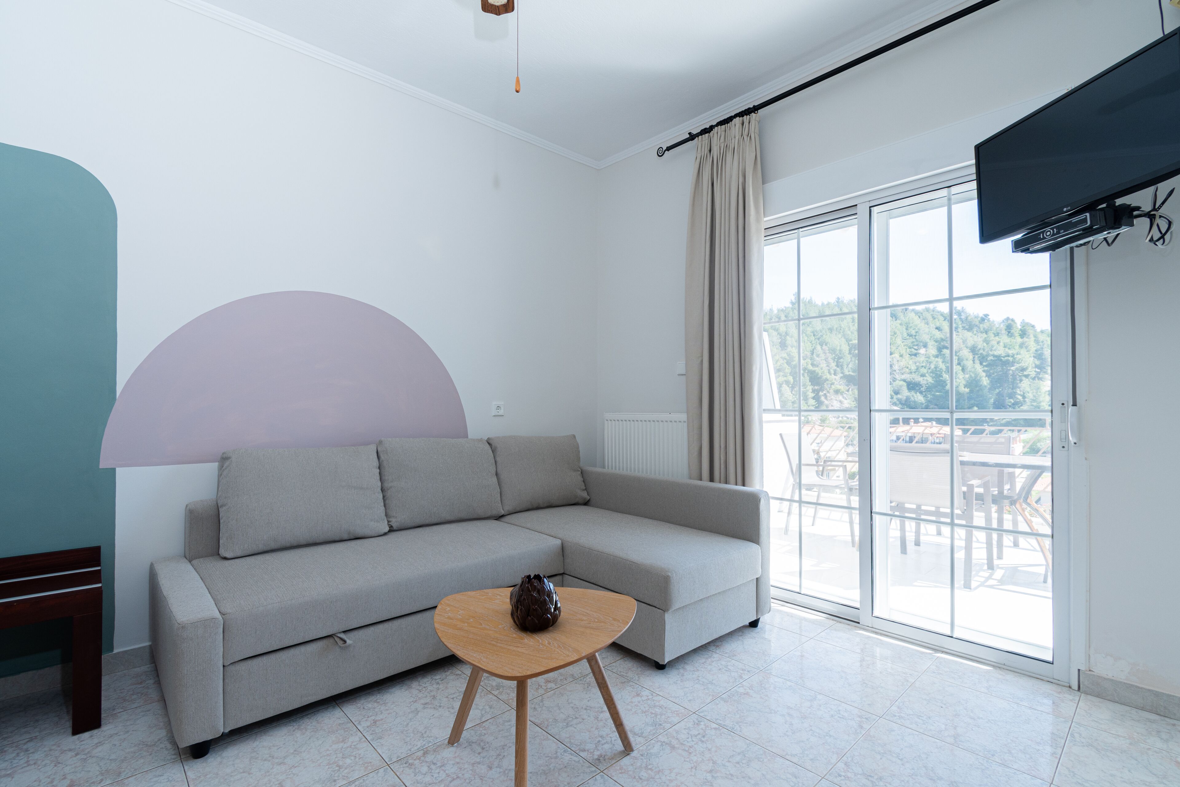 Una sala de estar moderna con un sofá gris, una mesa de centro de madera y un ventanal con vistas a la vegetación.