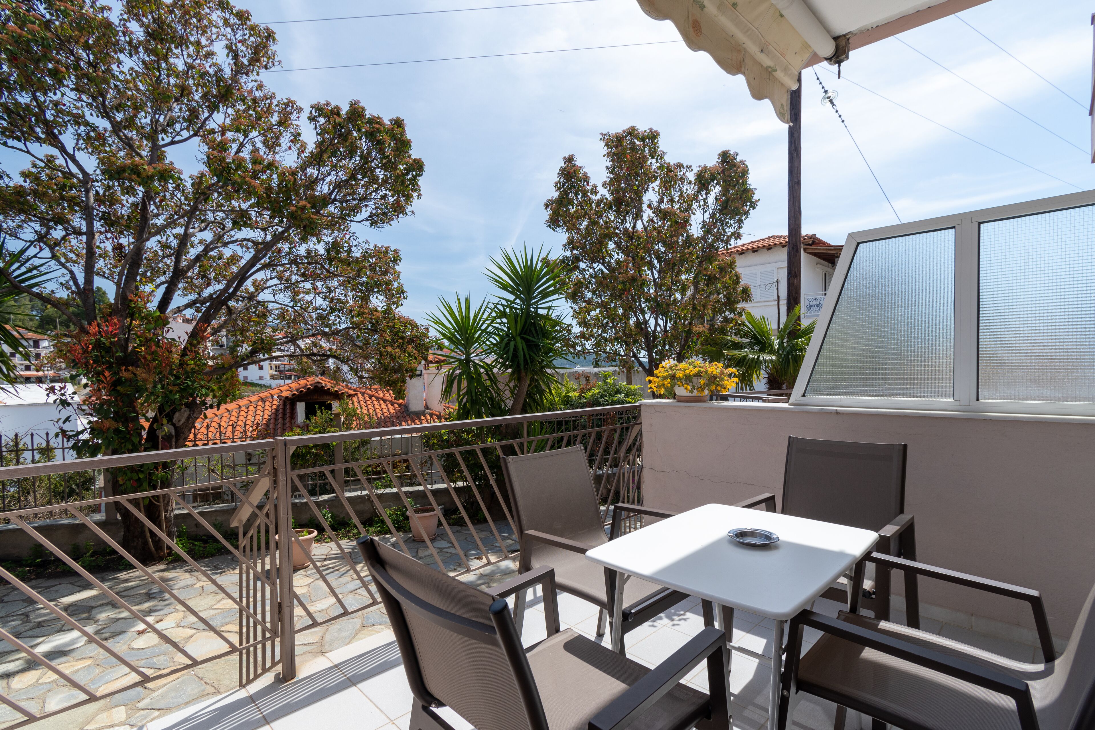 Un patio al aire libre con una mesa y sillas, rodeado por una baranda de metal y plantas en macetas.