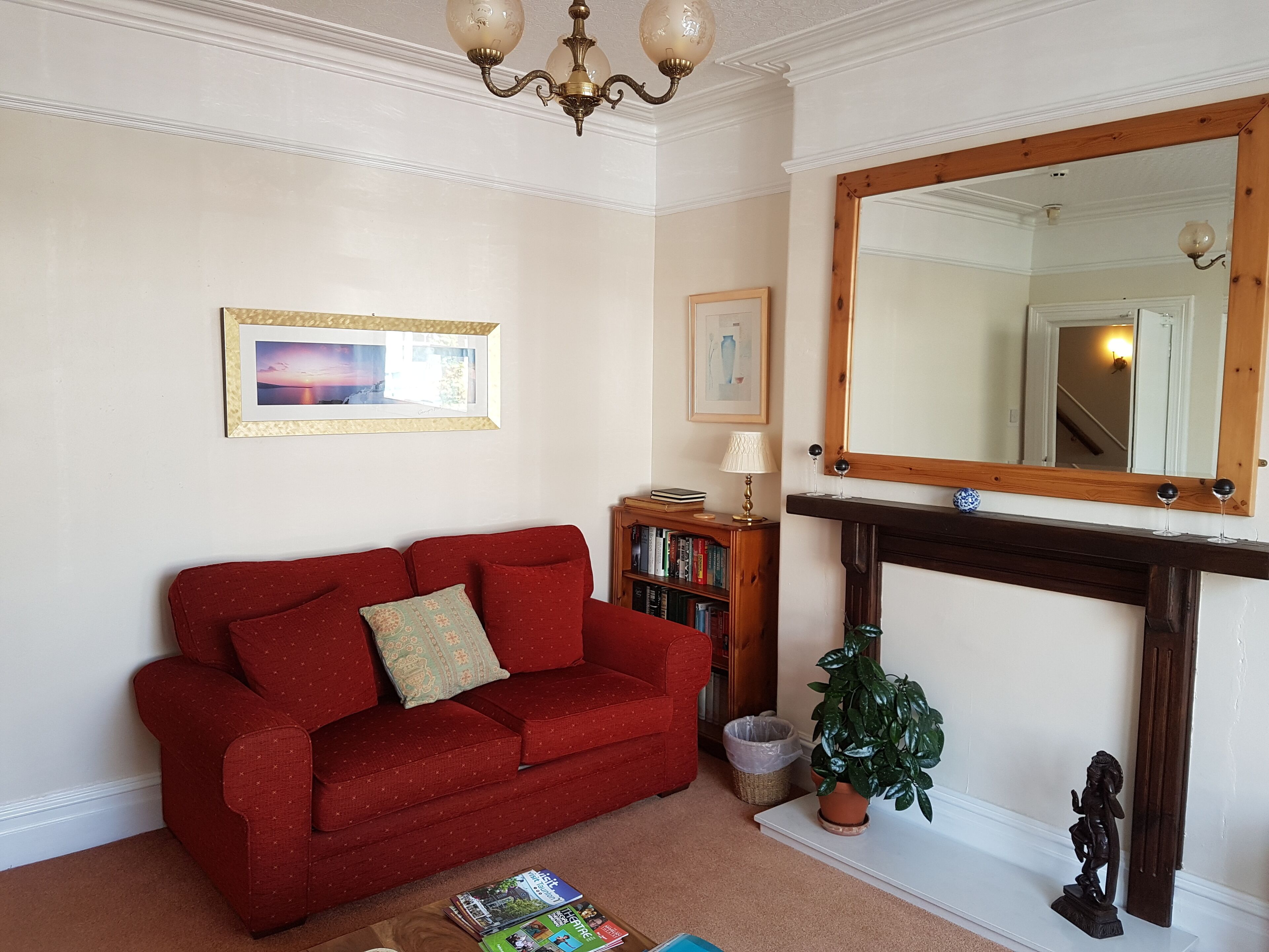 A living room with a red sofa, a fireplace, a mirror, and a bookshelf.