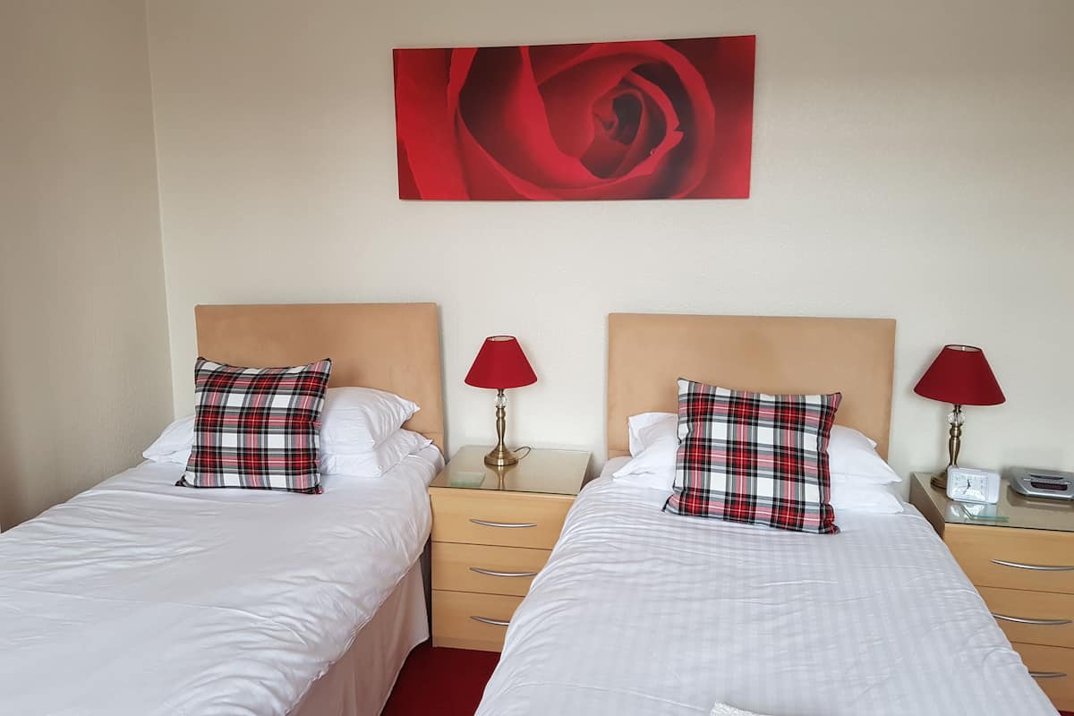 Habitación de hotel con dos camas, cada una con un cojín de cuadros y una lámpara roja.