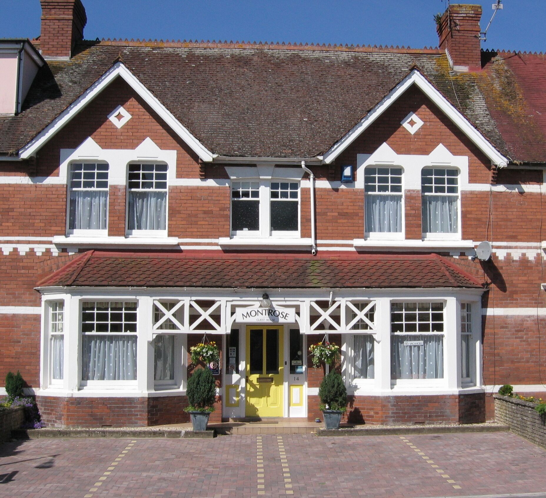A traditional brick building with a yellow entrance door, white window frames, and a symmetrical facade.