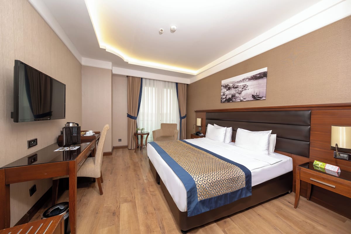 A hotel room with a large bed, a desk with a chair, a television, and a small table with a lamp.