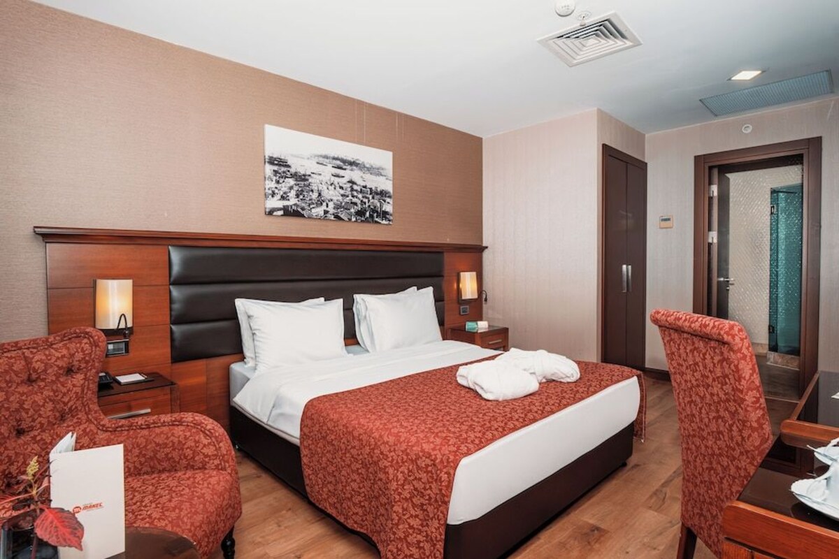 A hotel room with a large bed, two bedside tables, a desk with a chair, a mirror, and a picture on the wall.