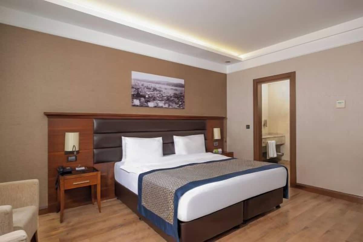 A hotel room with a large bed, bedside tables, a chair, a mirror, and a picture on the wall.