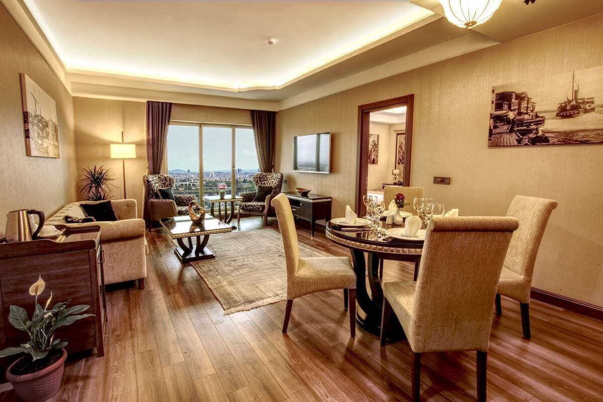 A spacious living room with a large dining table, comfortable seating, a TV, and a view of the city.