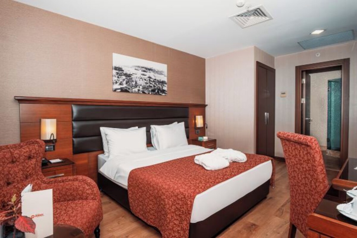 A hotel room with a large bed, two bedside tables, a nightstand, a chair, a desk, and a framed picture on the wall.