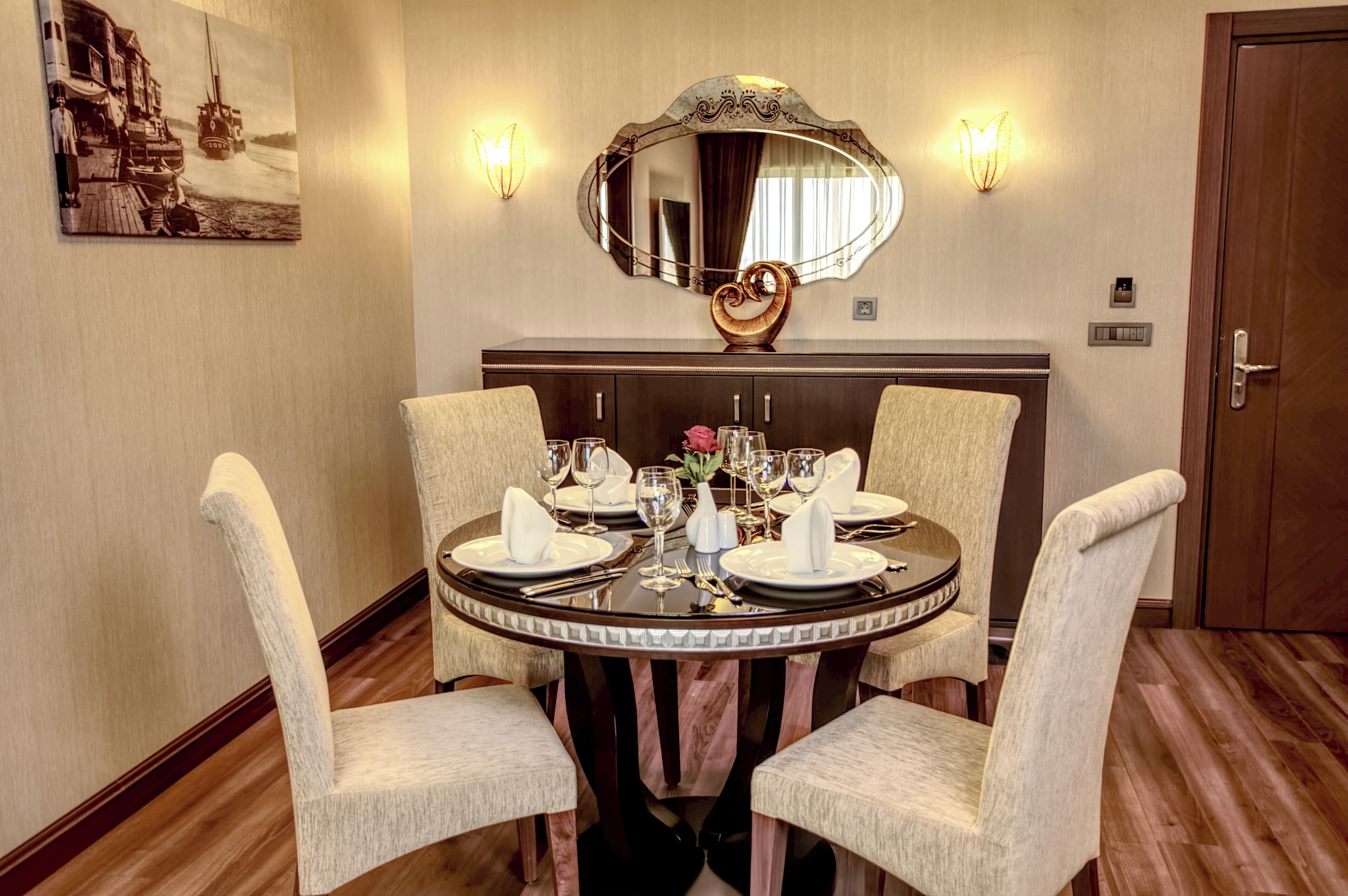 A dining table set for four with chairs, a mirror, and wall sconces.