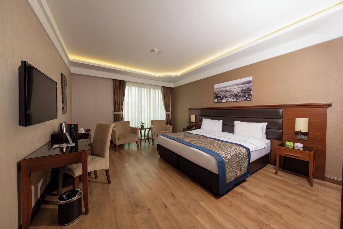 A hotel room with a large bed, a desk with a chair, a television, and a small table with a lamp.