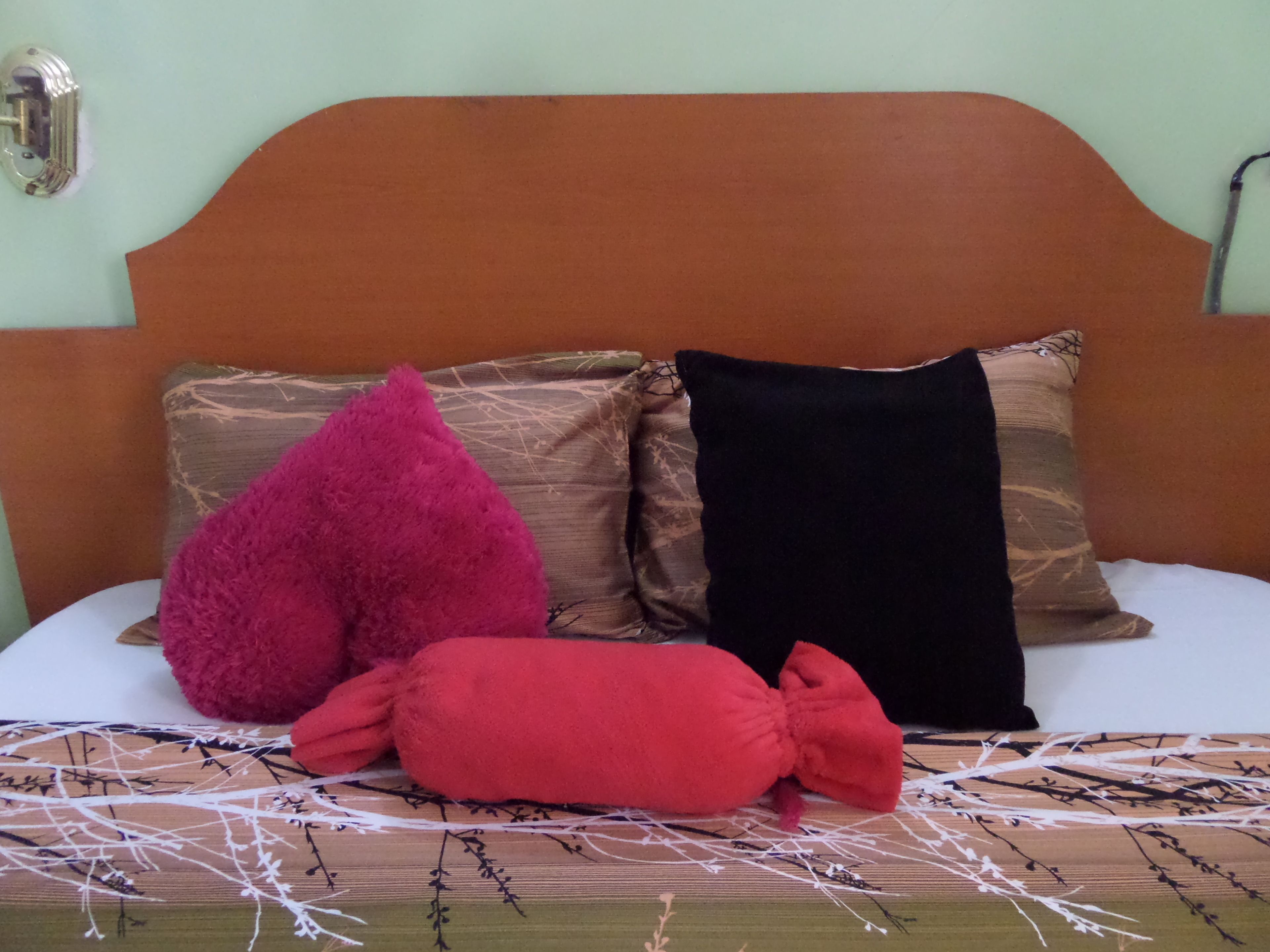 Cama com cabeceira marrom e três almofadas em cores diferentes.