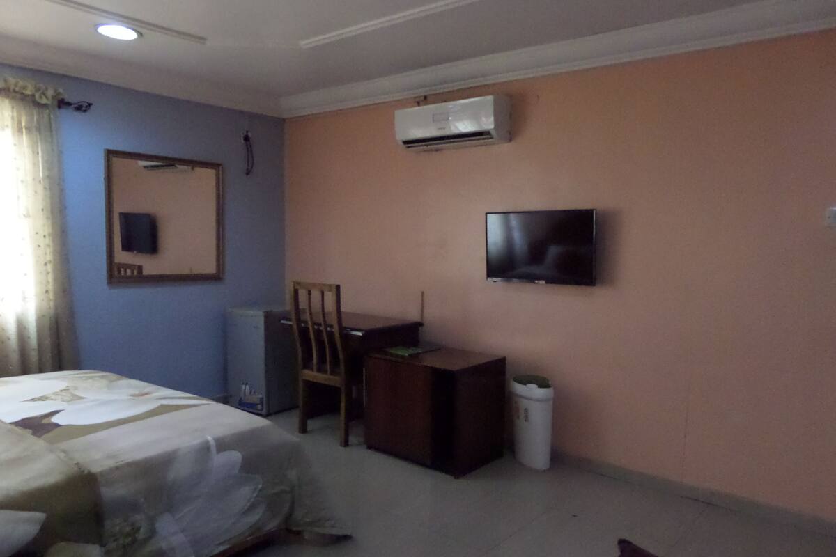Een hotelkamer met een bed, een bureau, een stoel, een televisie en een airconditioner aan de muur.