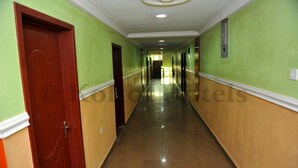 Un long couloir étroit aux murs verts et beige, avec une porte en bois sur le côté gauche et un luminaire au plafond.