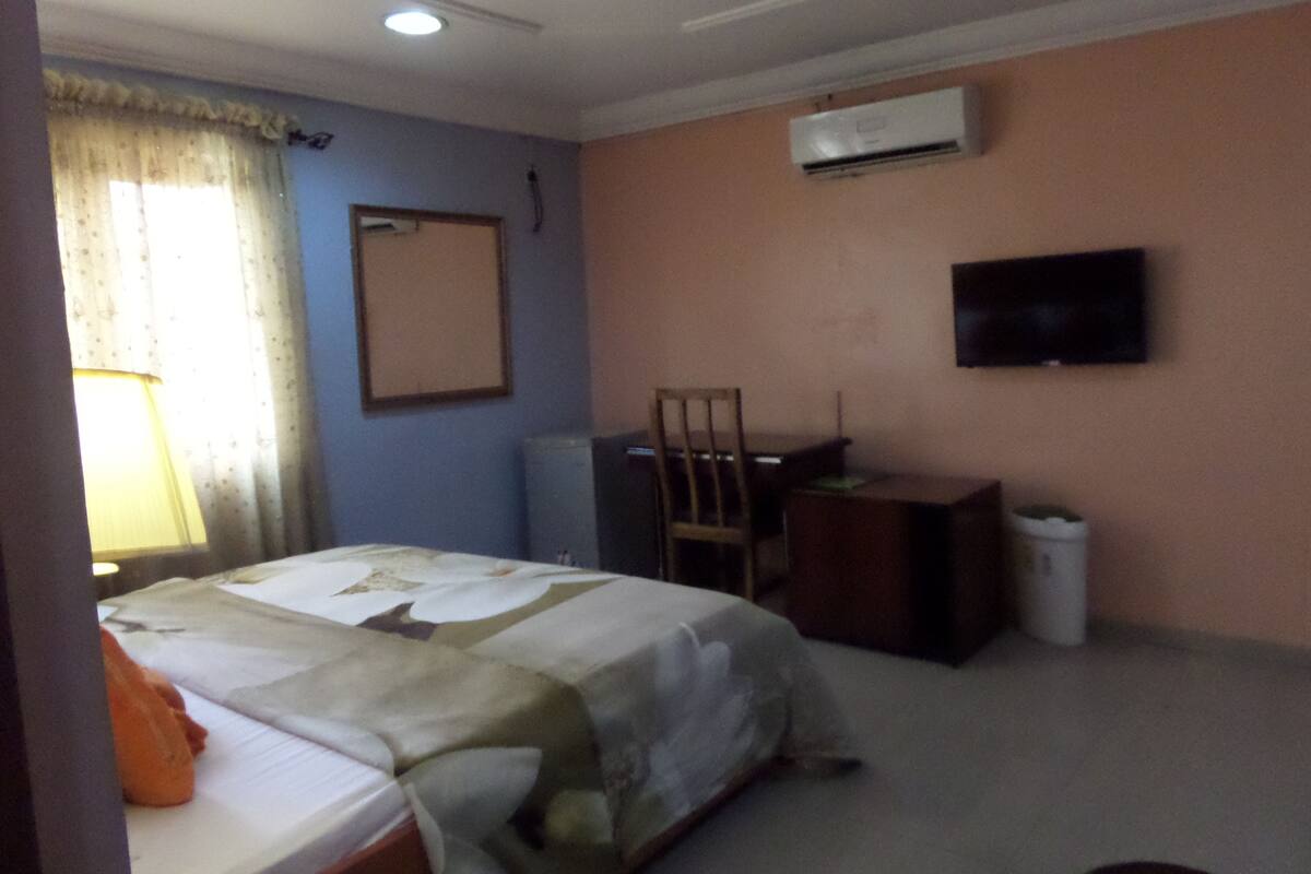 Een hotelkamer met een bed, een bureau, een stoel, een airconditioner en een televisie aan de muur.