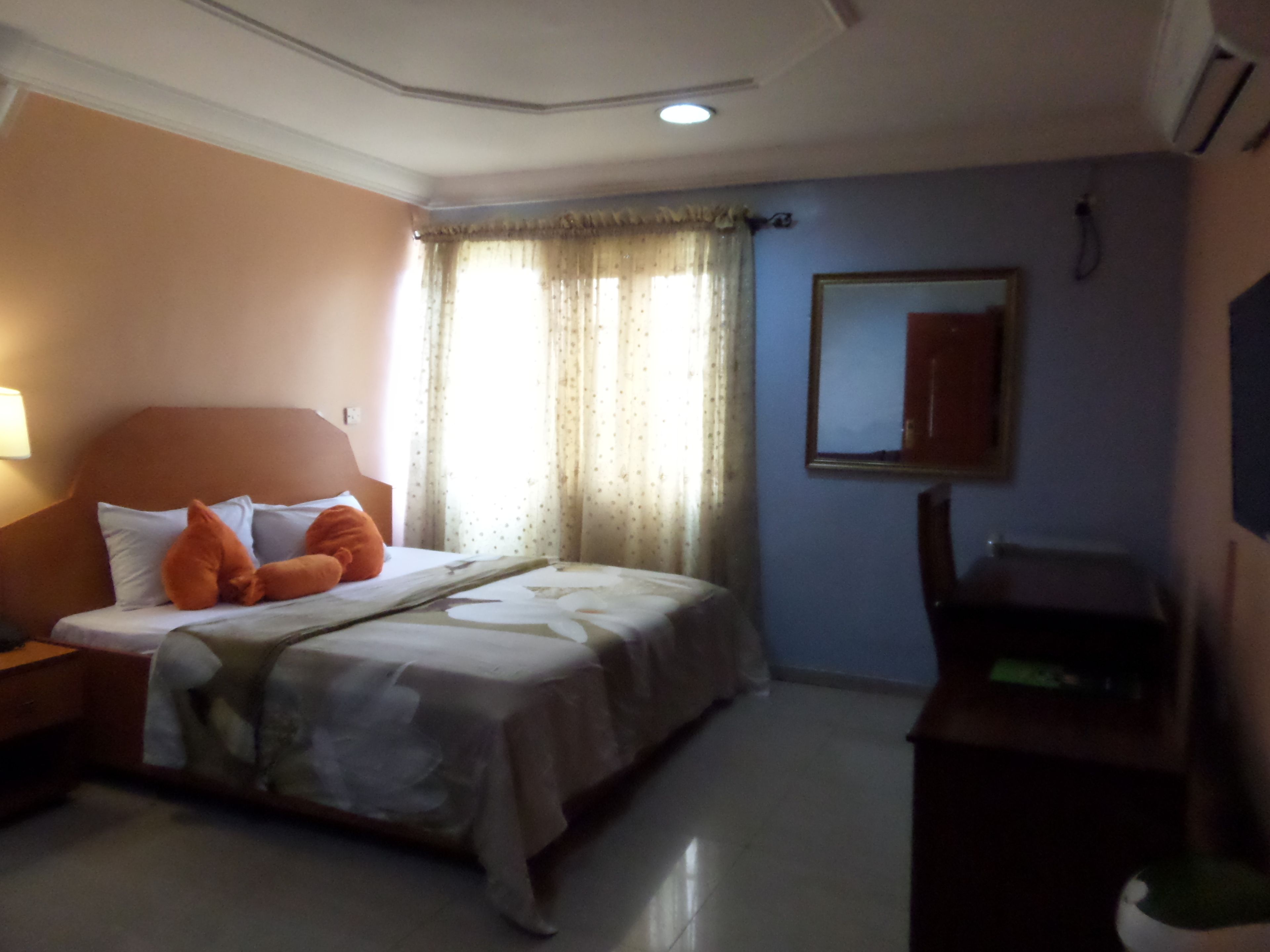 Une chambre d’hôtel comprenant un lit, une table de chevet, un bureau, une chaise, un miroir et une fenêtre avec des rideaux.