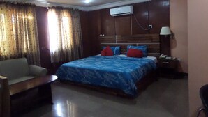 Une chambre d’hôtel équipée d’un lit, d’une chaise, d’une table de chevet, d’un climatiseur et d’une lampe.