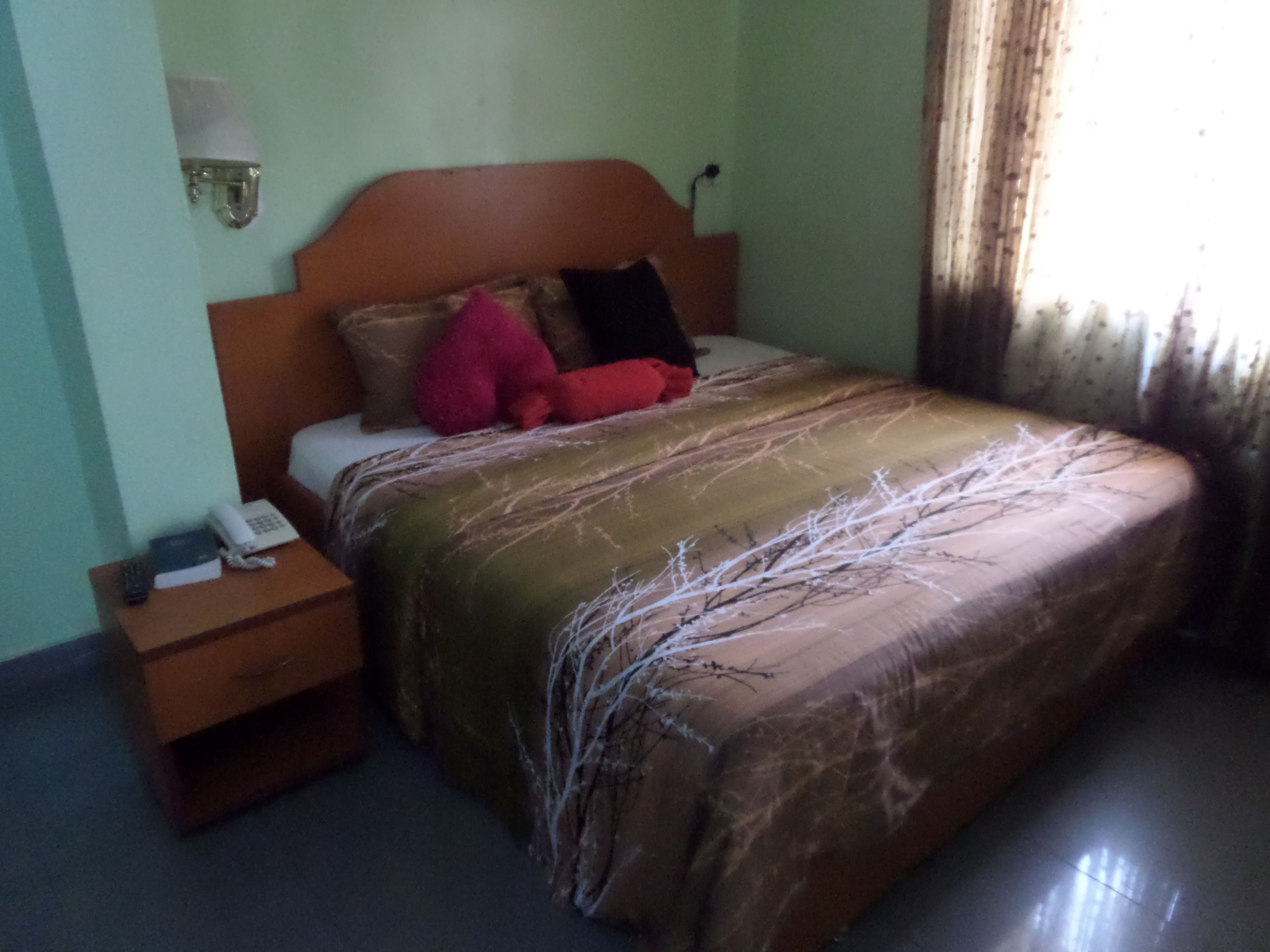 Quarto com cama de madeira, mesa de cabeceira com telefone e luminária na parede.