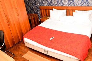 Relax in a cozy space with a neatly made bed, a comfortable chair, and a wooden wardrobe for your belongings.