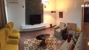 A living room with a flat-screen TV, yellow and grey sofas, a patterned rug, and a fireplace. - Koza Apartment (Lagos)