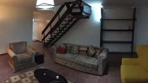 A living room with a sofa, two armchairs, a coffee table, a staircase, and a shelf. - Koza Apartment (Lagos)