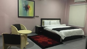 A bedroom with a bed, bedside table, chair, and a painting on the wall. - L'avalon Hotel and Suites (Lekki)