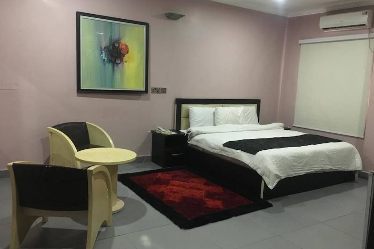 A bedroom with a bed, bedside table, chair, and a painting on the wall.