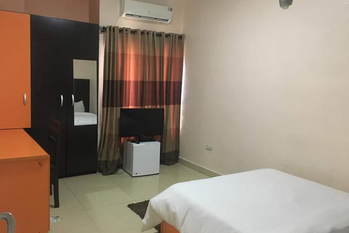 A room with a bed, a desk, a chair, an air conditioner, and a television.