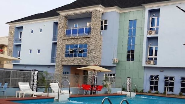 A hotel with a swimming pool, outdoor seating, and a stone facade. - L'avalon Hotel and Suites (Lekki)