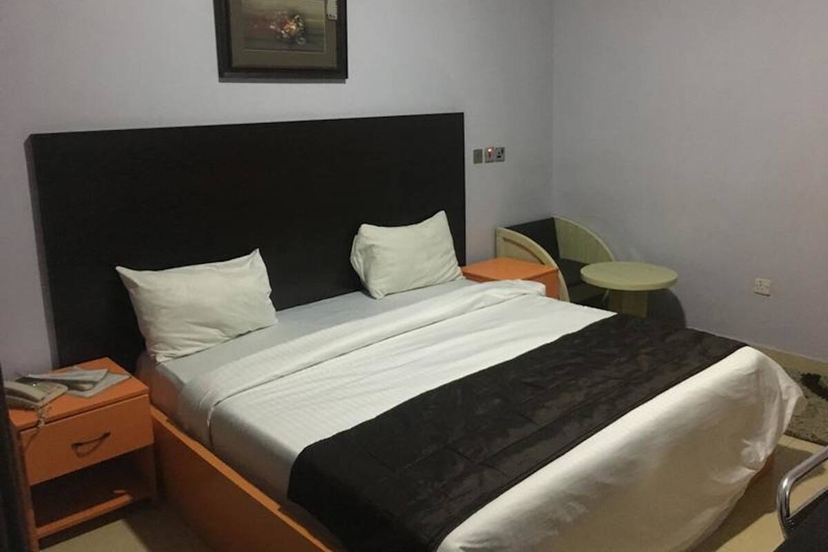 A hotel room with a large bed, a nightstand, a small table, and a chair.