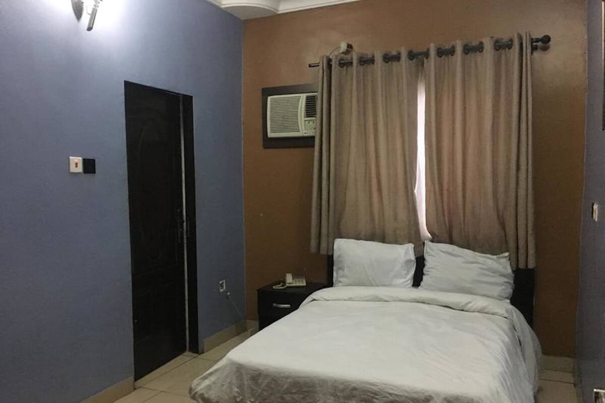 A bedroom with a bed, a nightstand, a door, and a wall-mounted air conditioner.