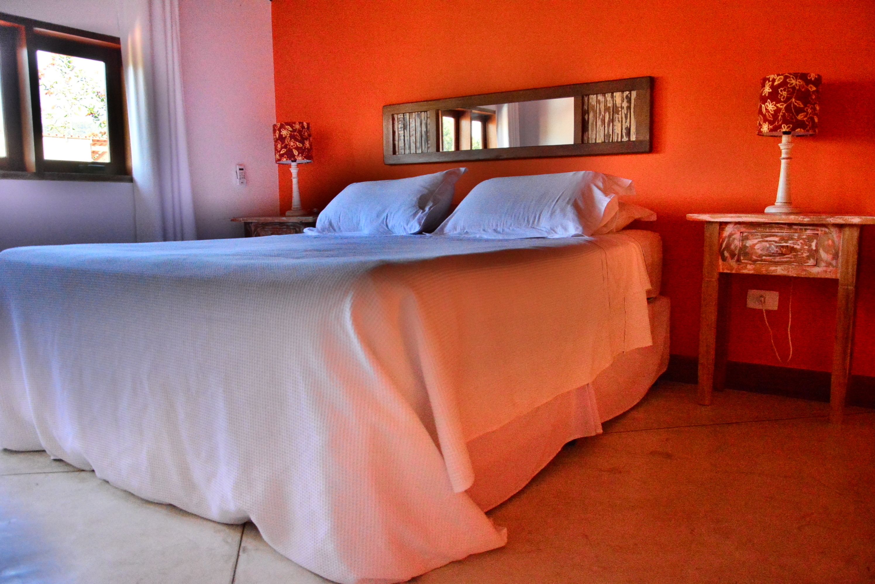 A bedroom with a large bed, a nightstand with a lamp, and a mirror on the wall.