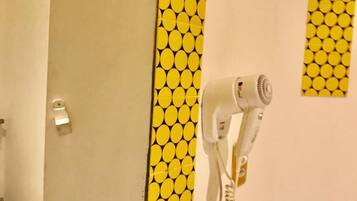 Un baño con pared amarilla estampada, un secador de pelo blanco montado en la pared y un espejo sobre un lavamanos.