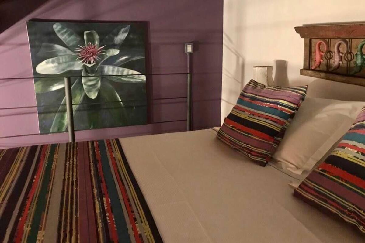 Quarto de hotel com uma grande obra de arte floral na parede, um tapete listrado e uma cama com almofadas listradas.