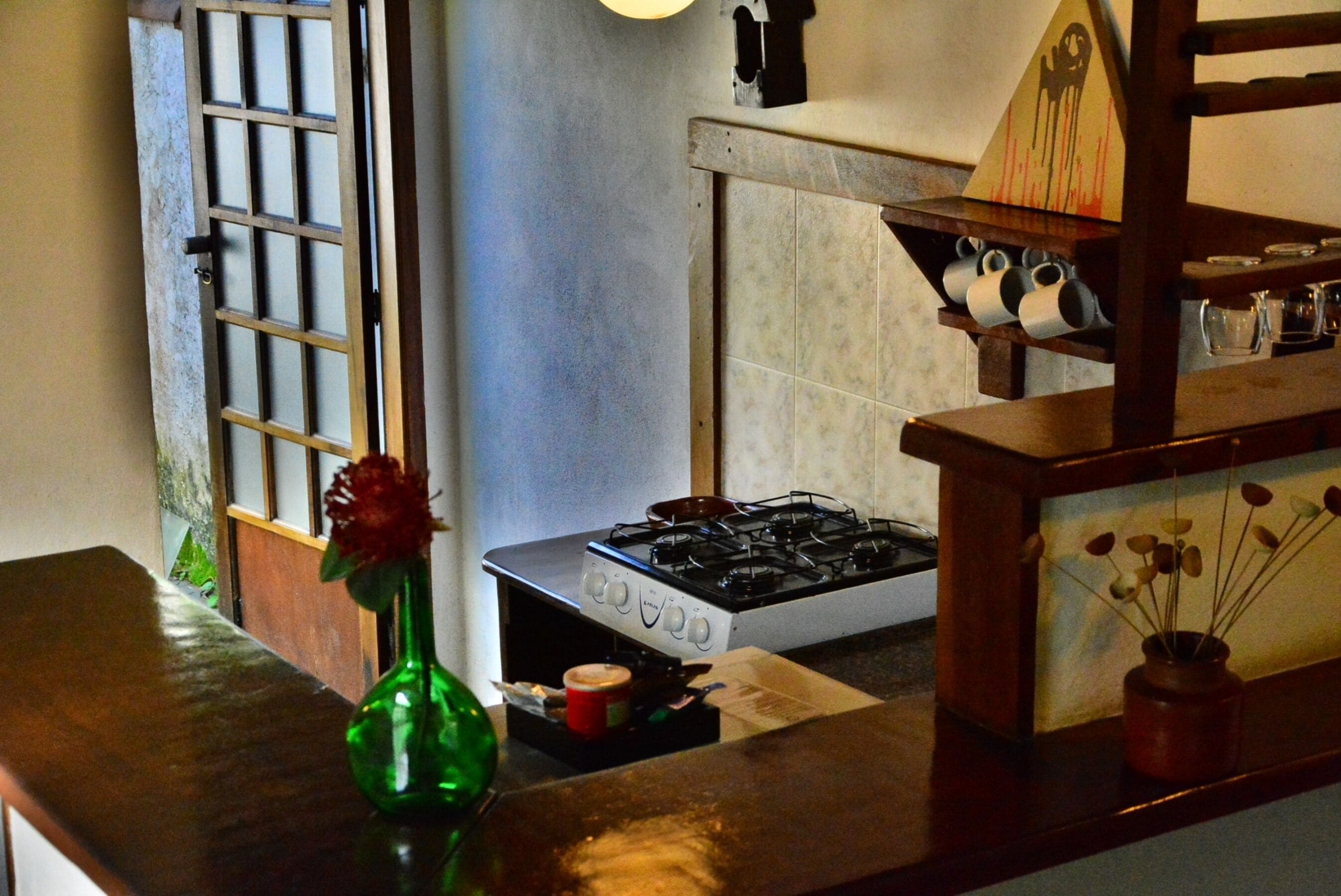 Una cocina con estufa a gas, un jarrón verde con una flor, y un estante de madera con utensilios de cocina.