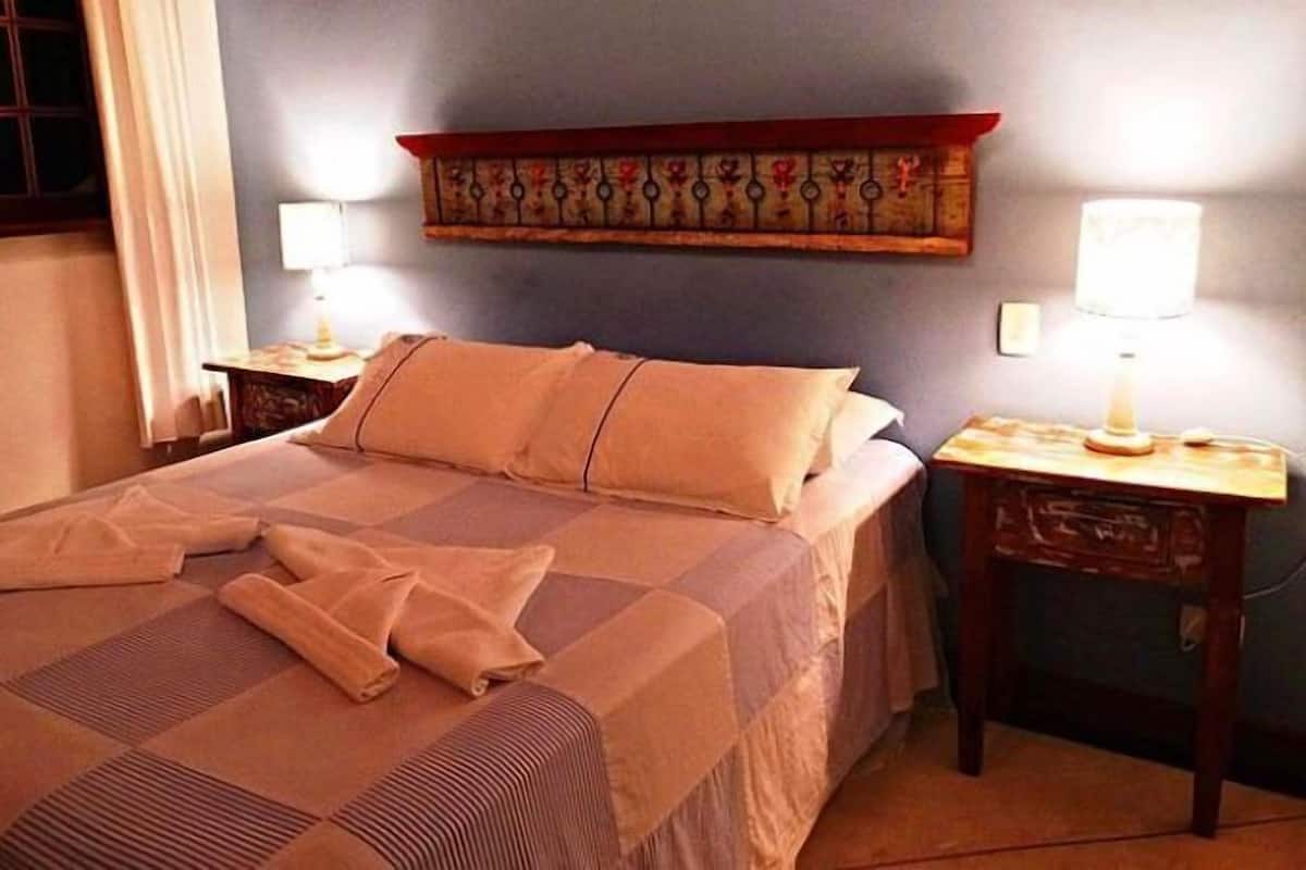 Uma cama bem arrumada com manta listrada, duas mesas de cabeceira com abajures e um adorno na parede acima da cama.