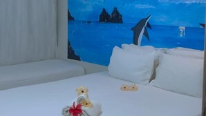 A hotel room with a bed, a painting of a whale and mountains, and an air conditioning unit. - Pousada Sao Silmares (Fernando de Noronha)