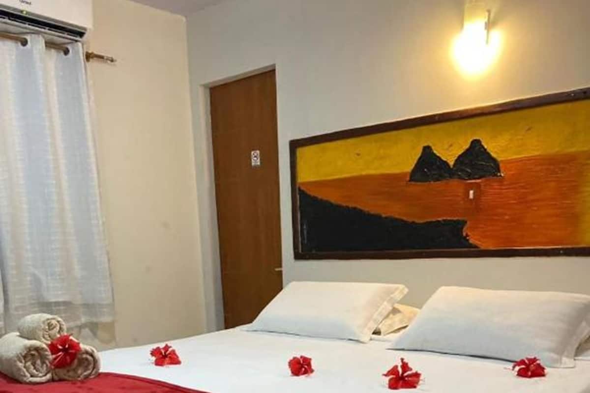 Une chambre d’hôtel avec un lit, un tableau représentant un coucher de soleil et une couverture rouge.