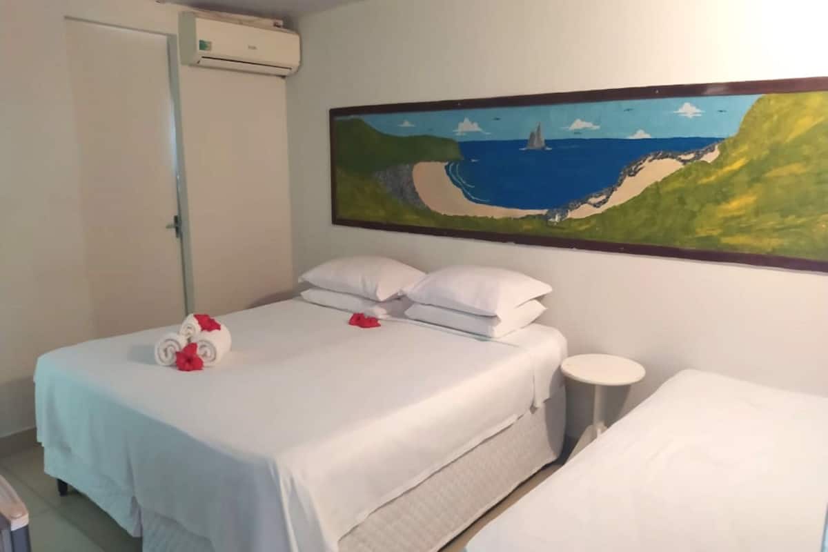 Une chambre d’hôtel avec un lit, une petite table de chevet et un tableau représentant un paysage côtier.