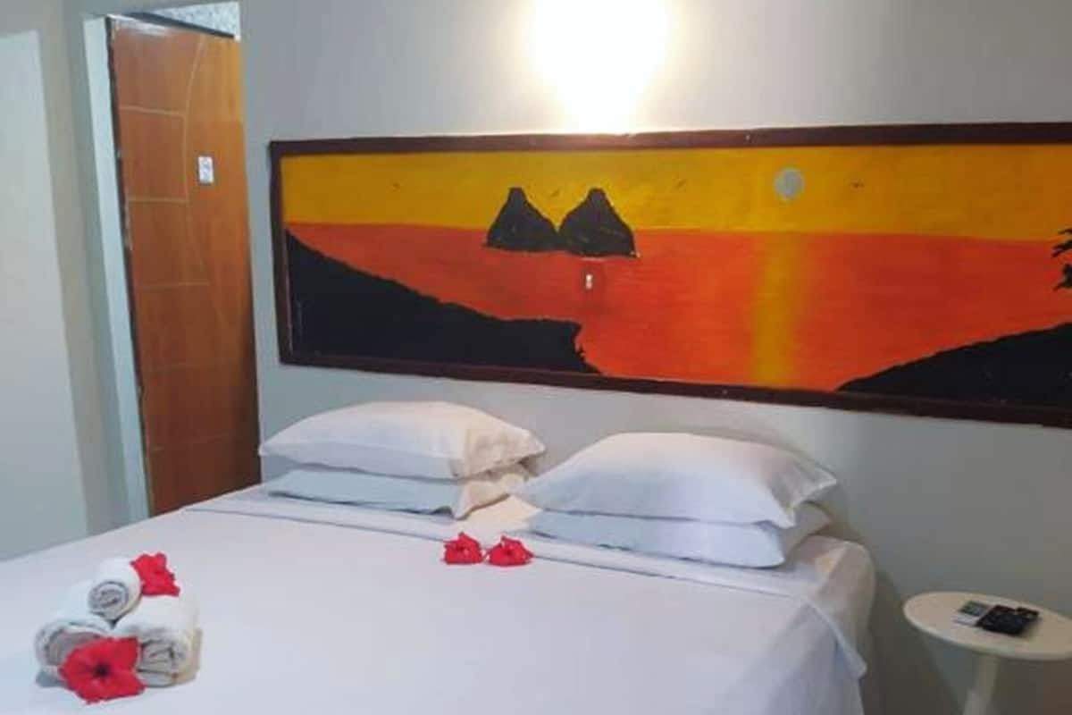 Une chambre d’hôtel avec un lit, des oreillers, une petite table de chevet et un tableau au mur.