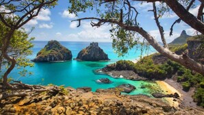 A coastal landscape with rocky terrain, clear turquoise waters, and two prominent rock formations. - Pousada Sao Silmares (Fernando de Noronha)