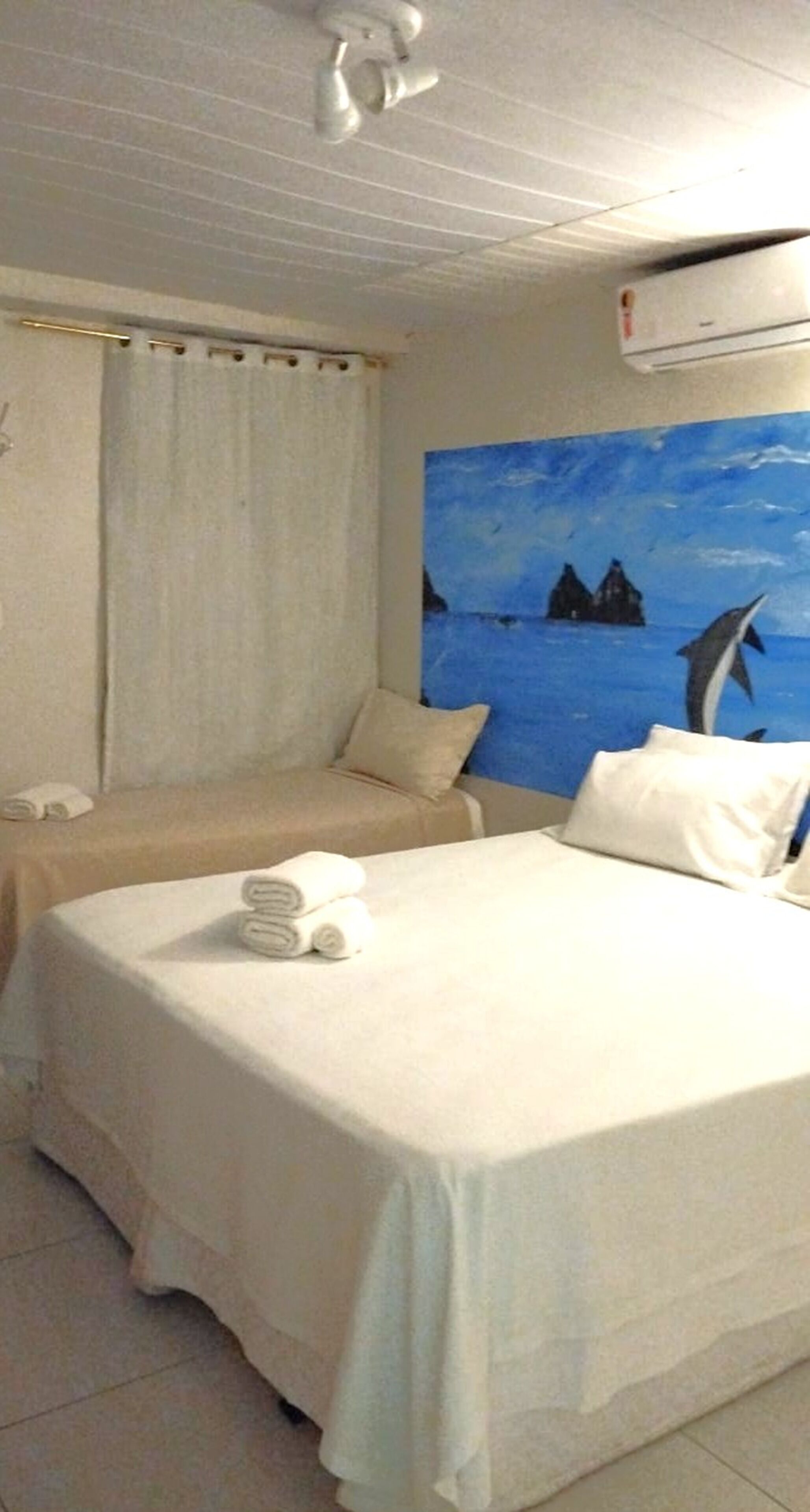 Una habitación de hotel con una cama, un cuadro de una escena marina y un equipo de aire acondicionado.