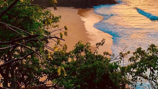 A coastal landscape with a sunset, rocky cliffs, and a beach. - Pousada Sao Silmares (Fernando de Noronha)