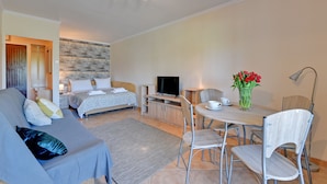 A modern hotel room with a sofa, a bed, a TV, a dining table with chairs, and a vase of flowers. - Muszelka Apartments - Very close to the beach and walking paths (Sopot)