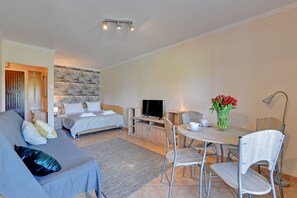 A modern hotel room with a sofa, a bed, a TV, a dining table with chairs, and a vase of flowers. - Muszelka Apartments - Very close to the beach and walking paths (Sopot)