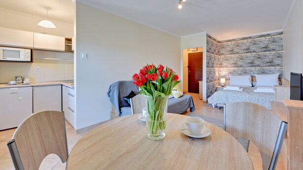 A modern hotel room with a kitchen, a dining area with a vase of red tulips, and a bed with a stone wall. - Muszelka Apartments - Very close to the beach and walking paths (Sopot)