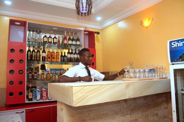Zona de bar con mostrador, estantes con botellas de licores y un cartel que dice "Shin".