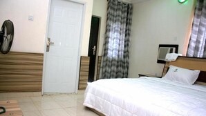 Un dormitorio con una cama, un escritorio, una silla, una puerta, un ventilador y una cortina.