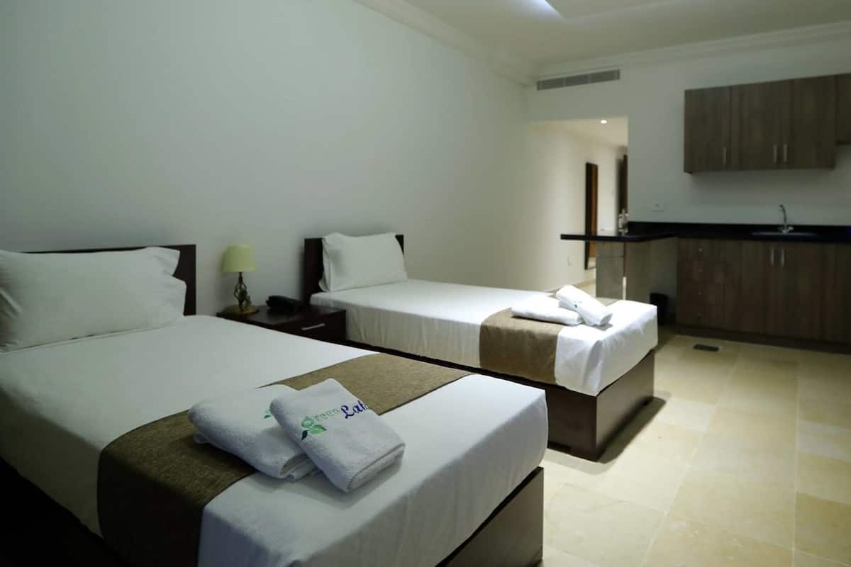 Een hotelkamer met twee bedden, een kleine keuken en een bureau.