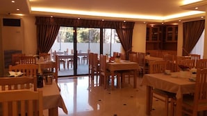 Un espace repas comprenant plusieurs tables et chaises, de grandes fenêtres avec des rideaux et un plafond doté d’un éclairage encastré.
